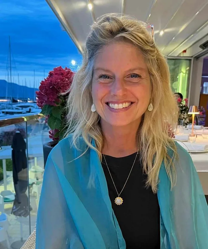 Elizabeth Binyon smiling in a turquoise scarf by a harbour at dusk