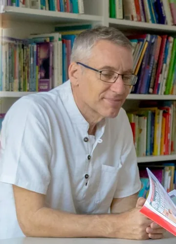 Neil Amas reading at a desk in front of full bookshelves