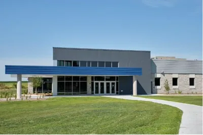 A modern single storey school building with a blue canopy and a wide lawn